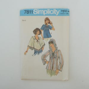 May include: Vintage Simplicity sewing pattern number 7811 for three different blouses. The pattern includes a blue, white, and striped blouse with a ruffled neckline. The pattern is for size 8.