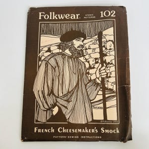 May include: A brown and cream paper sewing pattern envelope titled Folkwear 102 French Cheesemaker's Smock. The front features a line drawing of a person wearing a smock and beret, holding a staff, with a flock of sheep in the background.