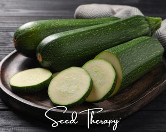 May include: Two whole dark green zucchinis with speckled skin and two sliced zucchini rounds resting on a wooden platter. The text Seed Therapy is printed in white cursive script at the bottom of the image, centered below the vegetables.