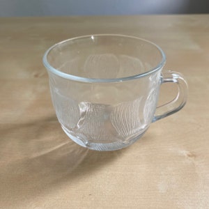 Pu&ograve; includere: Una tazza di vetro trasparente con un design testurizzato. La tazza ha una forma arrotondata e un manico.