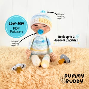 May include: A crocheted baby doll wearing a blue and yellow striped hat and outfit, with a blue pacifier. The doll is holding two pacifiers. Text on the image says "Low-sew PDF Pattern" and "Dummy Buddy".