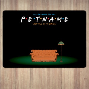 以下が含まれることがあります： 人気テレビ番組にインスパイアされた、カラフルな文字で「PET NAME」と書かれた黒いペット用プレースマット。デザインには、漫画のオレンジ色のソファ、ランプ、「I'll be there for you...」と「Just fill up my bowls.」というフレーズが含まれています。