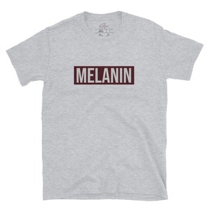 May include: A heather grey t-shirt with a maroon rectangle that says "MELANIN" in white text.