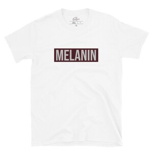 May include: White t-shirt with a maroon rectangle that says "MELANIN" in white letters.