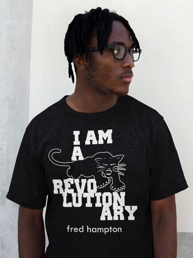 May include: A black t-shirt with a white graphic of a black panther and the text "I AM A REVOLUTIONARY fred hampton".