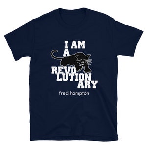 May include: A navy blue t-shirt with white text that reads "I am a revolutionary" and a black panther graphic. The text "fred hampton" is printed below the graphic.