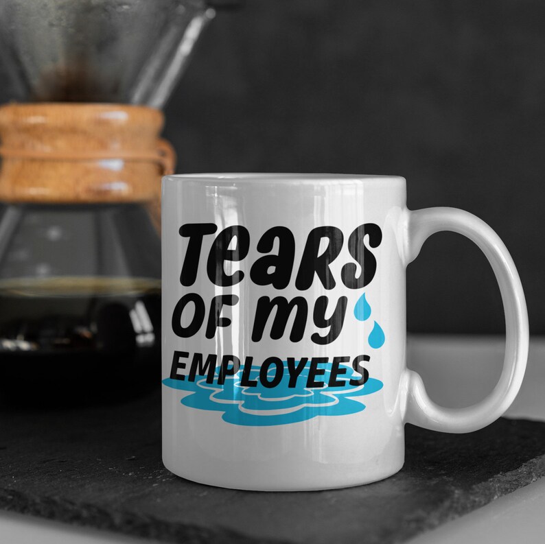 Puede incluir: Taza de cer&aacute;mica blanca con el texto "Tears of my Employees" en negro y azul. La taza tiene un asa y un dise&ntilde;o de l&aacute;grimas azules y un charco. Una cafetera est&aacute; en el fondo.