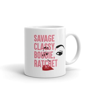 Peut inclure: Une tasse à café en céramique blanche avec un motif graphique rose et noir. Le motif présente les mots "Savage, Classy, Bougie, Ratchet" et une image stylisée d'un œil et de lèvres de femme.