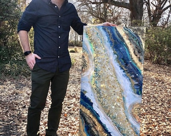 Puede incluir: Una persona se encuentra frente a una gran pieza de arte abstracto de resina. La obra de arte presenta un esquema de color azul, blanco y dorado con un diseño en espiral y en capas. La obra de arte mide aproximadamente 100 cm de alto.