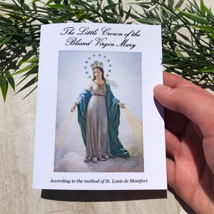 May include: A white booklet with the title "The Little Crown of the Blessed Virgin Mary" and a picture of the Virgin Mary in a blue and white robe. The text at the bottom reads "According to the method of St. Louis de Montfort."