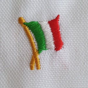 Può includere: Una piccola bandiera italiana ricamata con strisce verdi, bianche e rosse su uno sfondo bianco.