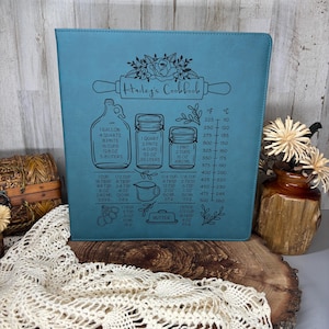 May include: A teal-colored binder featuring a black laser-engraved design of a kitchen conversion chart. The graphic includes a rolling pin, floral accents, a jug, jars, a measuring cup, a butter stick, and a temperature conversion scale.