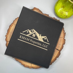 May include: Black leather binder with gold stitching and a gold engraved logo of three houses with the text "KMAM Properties, LLC".
