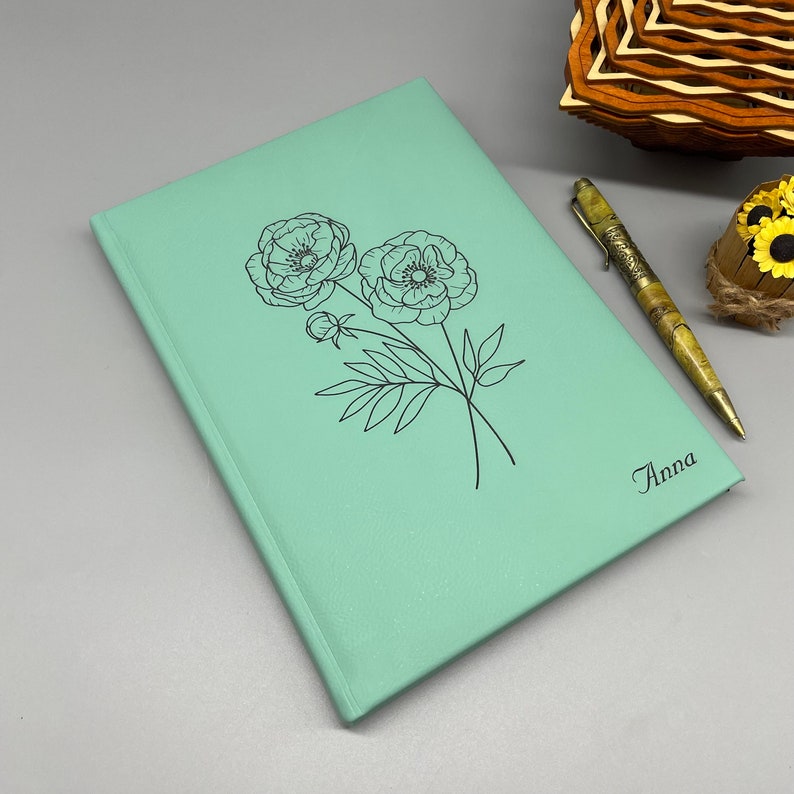 May include: A light green leather journal with a floral design and the name "Anna" embossed on the cover.