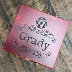 May include: A red wooden box with a gold latch. The box has a black spade symbol inside a circle and the name "Grady" engraved on the front.