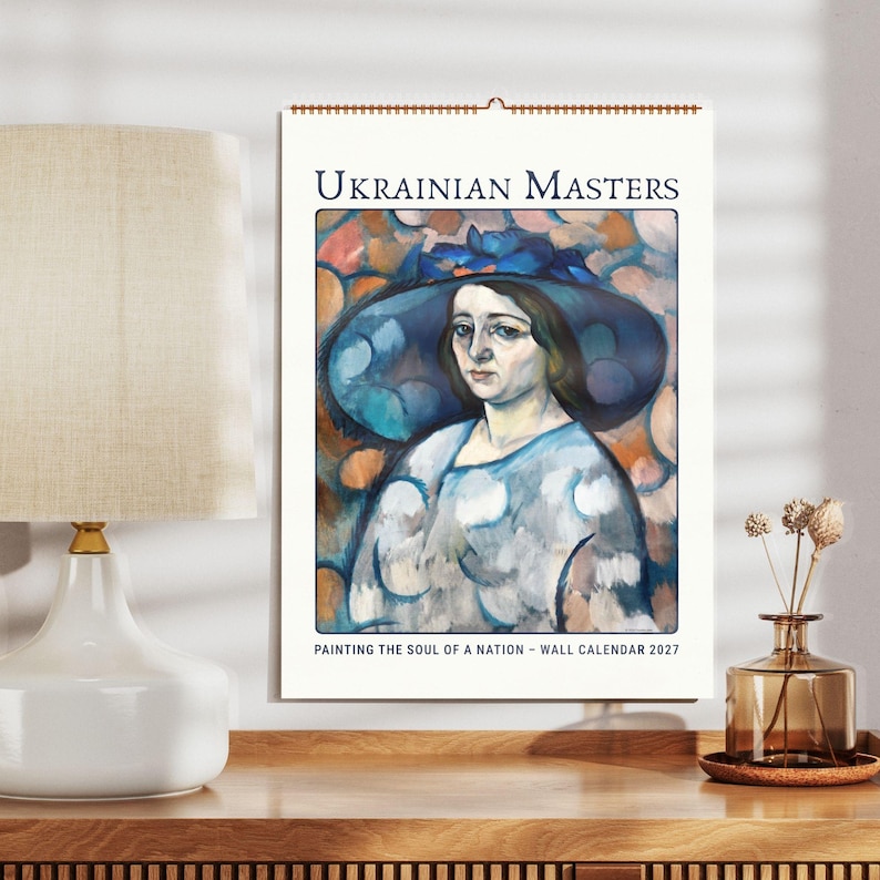 Może przedstawiać: Kalendarz ścienny zatytułowany Ukrainian Masters Painting the Soul of a Nation Wall Calendar 2027. Okładka przedstawia obraz osoby w dużym niebieskim kapeluszu i wzorzystej bluzce na tle abstrakcyjnych pomarańczowych i niebieskich k&oacute;ł.