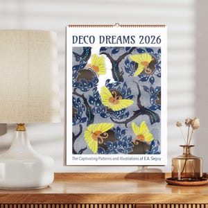 Könnte beinhalten: Ein Kalender mit einem farbenfrohen Art-Deco-Design mit gelben Schmetterlingen und blauen und grünen Blättern. Der Kalender trägt den Titel "Deco Dreams 2026" und enthält den Text "The Captivating Patterns and Illustrations of E.A. Seguy".