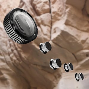 May include: A collection of black and silver objects, including a large, round, lens-like component and several smaller, cylindrical components with textured black tops. The objects appear to be floating against a blurred, rocky background.