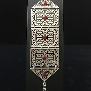 May include: Silver bracelet with four red gemstone accents and a geometric design. The bracelet has a chain link extension.