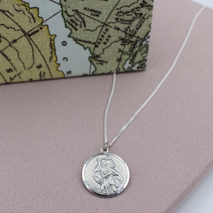 Op de afbeelding: Zilveren ketting met een ronde hanger met een gedetailleerd beeld van Sint Christoffel. De hanger heeft een getextureerde rand.