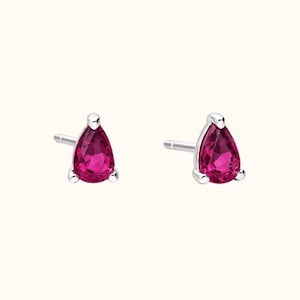 May include: A pair of stud earrings with a pear-shaped, magenta gemstone set in silver metal. The earrings have a simple, elegant design, suitable for everyday wear or special occasions.