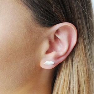 Op de afbeelding: Een paar zilveren veren oorbel studs. De oorbellen zijn klein en delicaat, en ze hebben een eenvoudig veren ontwerp.