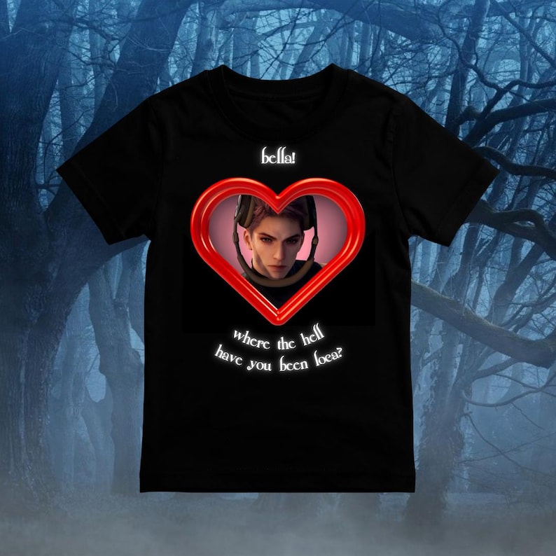 Puede incluir: Una camiseta negra de manga corta con un marco rojo en forma de coraz&oacute;n que contiene la ilustraci&oacute;n de una persona de pelo corto con auriculares. Sobre el coraz&oacute;n aparece el texto "bella!" y debajo "where the hell have you been loca?"