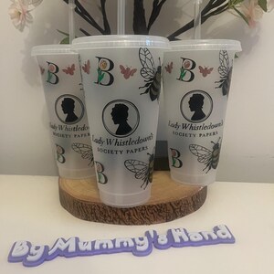 May include: Three clear plastic tumblers with lids and straws, decorated with a bee, butterfly, and the letter "B". Each tumbler features a silhouette and the text "Lady Whistledown's Society Papers". The tumblers are displayed on a wooden slice.