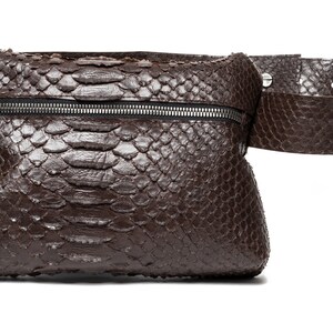 May include: A brown leather fanny pack with a snakeskin pattern and a zipper closure. The bag has a wide brown leather belt.