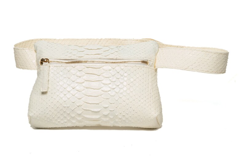 May include: A white leather fanny pack with a zipper closure and a snakeskin pattern.