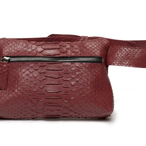 May include: A burgundy leather fanny pack with a snakeskin pattern and a zipper closure.