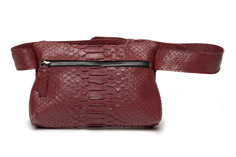May include: A burgundy leather fanny pack with a snakeskin pattern and a zipper closure.