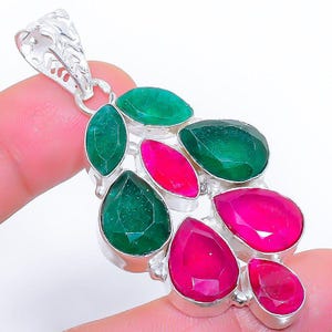 May include: A silver pendant featuring a cluster of faceted gemstones. The pendant showcases a mix of green and magenta-pink stones in various shapes, including teardrops and ovals. The pendant has a decorative bail.