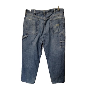 May include: A pair of blue denim work pants featuring a high-rise waist, a V-shaped back yoke, two large patch pockets on the rear, and a utility loop on the side. The jeans have a faded wash, belt loops, and a small rectangular brand label.