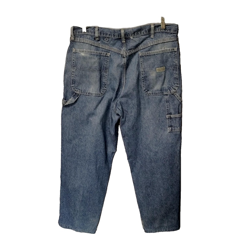 May include: A pair of blue denim work pants featuring a high-rise waist, a V-shaped back yoke, two large patch pockets on the rear, and a utility loop on the side. The jeans have a faded wash, belt loops, and a small rectangular brand label.