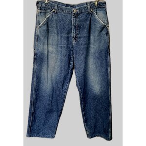 May include: A pair of medium-wash blue denim carpenter jeans featuring a high-waisted fit, a button fly closure, and reinforced side pockets. The fabric displays a faded texture with lighter blue highlights throughout the front panels.