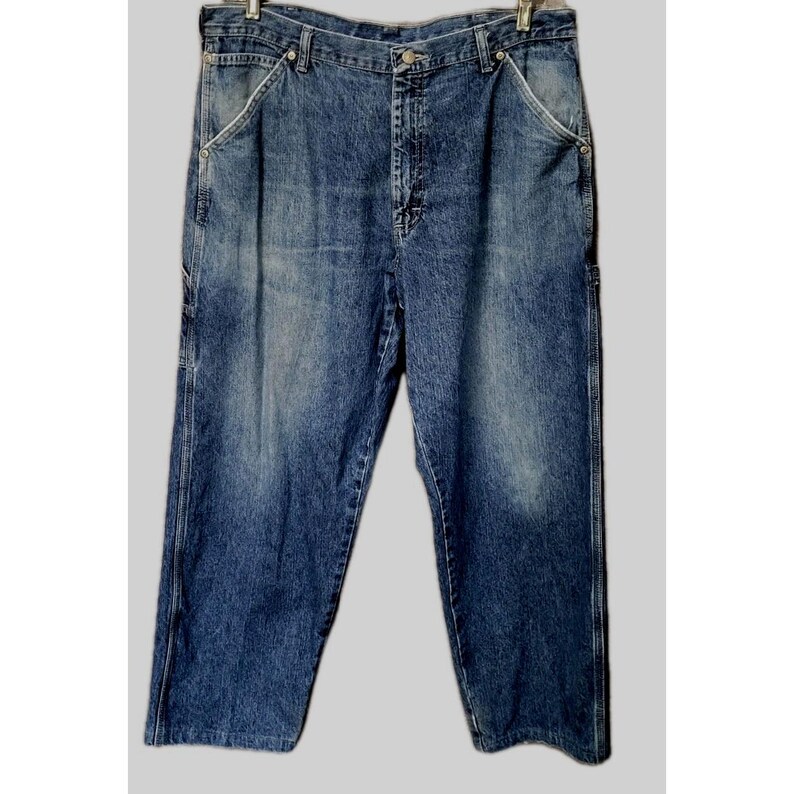 May include: A pair of medium-wash blue denim carpenter jeans featuring a high-waisted fit, a button fly closure, and reinforced side pockets. The fabric displays a faded texture with lighter blue highlights throughout the front panels.