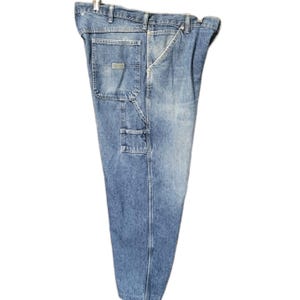 May include: Light blue denim carpenter pants featuring a high-waisted design, a metal button closure, belt loops, and multiple utility pockets on the side. The fabric displays a faded wash with visible stitching and a rectangular brand patch.