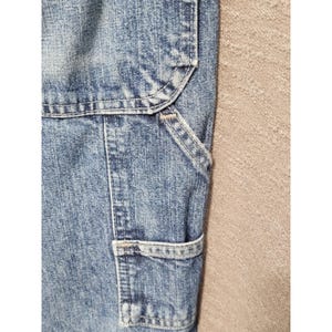 May include: A pair of blue denim pants featuring a light acid wash finish, reinforced stitching, and a utility pocket design. The fabric displays a textured, mottled blue and white appearance with visible seams and heavy-duty construction details.