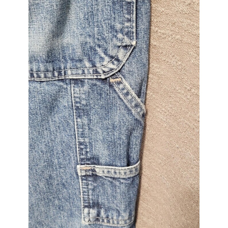 May include: A pair of blue denim pants featuring a light acid wash finish, reinforced stitching, and a utility pocket design. The fabric displays a textured, mottled blue and white appearance with visible seams and heavy-duty construction details.