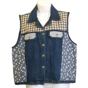 May include: A sleeveless denim vest featuring a dark blue wash, a collar, and a front button closure with metallic buttons. The garment includes panels of brown and white plaid fabric at the shoulders and blue floral print fabric on the sides.