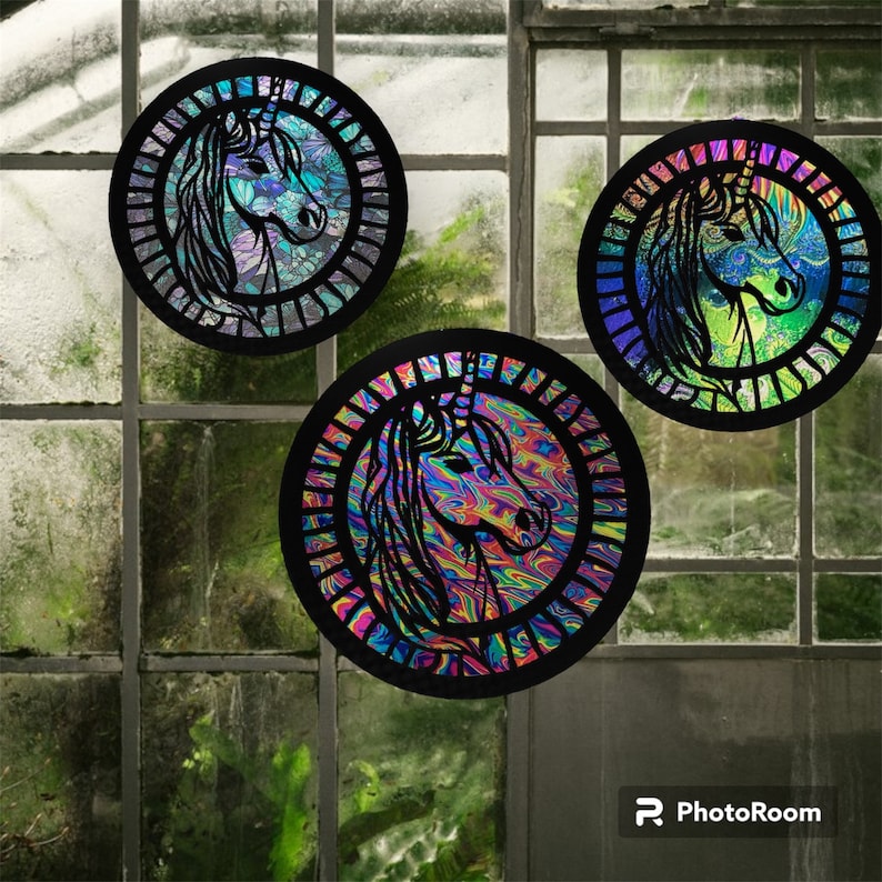 May include: Three round, black framed, iridescent, stained glass ornaments featuring a unicorn silhouette. The unicorn silhouettes are cut out of the glass and have a black outline. The background of the ornaments is a swirling pattern of blue, green, and purple.