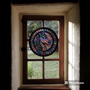 May include: A colorful stained glass window with a unicorn design. The unicorn is surrounded by a rainbow of colors and is set against a black background.