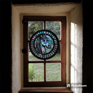 May include: A black metal unicorn silhouette with a stained glass design in shades of blue, purple, and green, hanging in a window.