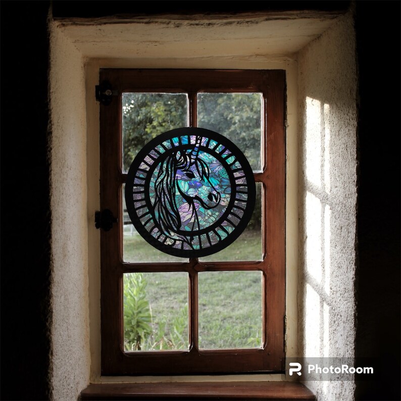 May include: A black metal unicorn silhouette with a stained glass design in shades of blue, purple, and green, hanging in a window.