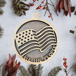 May include: A wooden ornament featuring a cutout of the American flag with the words "We the People" inscribed around the edge.
