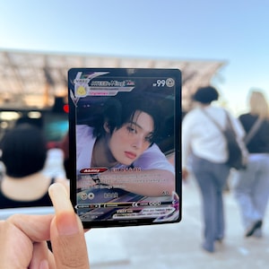 Puede incluir: Una tarjeta coleccionable con Mingi de ATEEZ. La tarjeta tiene un borde negro con el texto "VMAX" y "Dynamax". La ilustraci&oacute;n de la tarjeta representa a una persona con cabello oscuro. La tarjeta tambi&eacute;n incluye el texto "FIX ON & ON" y "ROAR 60."