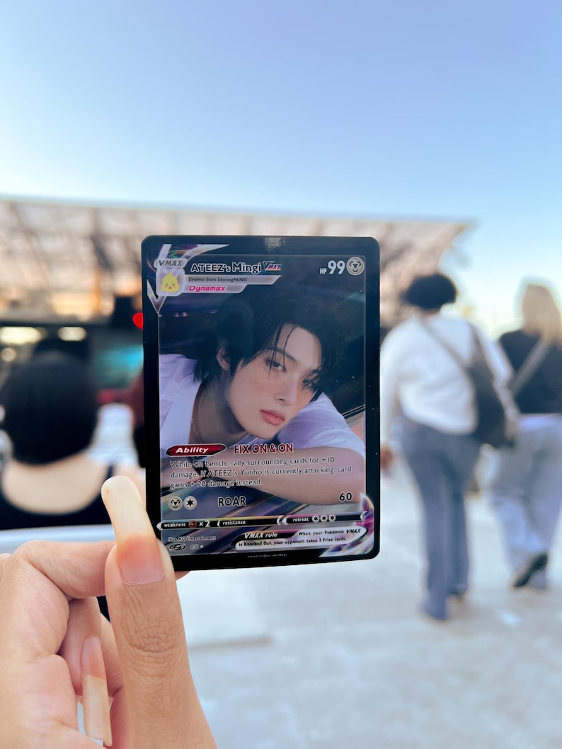 Puede incluir: Una tarjeta coleccionable con Mingi de ATEEZ. La tarjeta tiene un borde negro con el texto "VMAX" y "Dynamax". La ilustraci&oacute;n de la tarjeta representa a una persona con cabello oscuro. La tarjeta tambi&eacute;n incluye el texto "FIX ON & ON" y "ROAR 60."