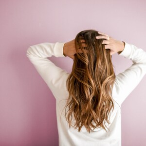 K&ouml;nnte beinhalten: Ein lang&auml;rmeliges wei&szlig;es Sweatshirt, getragen von einer Person mit langem, welligem, hellbraunem Haar mit goldenen Highlights. Das Haar f&auml;llt &uuml;ber den R&uuml;cken und die H&auml;nde befinden sich oben auf dem Kopf und ber&uuml;hren das Haar am Oberkopf.