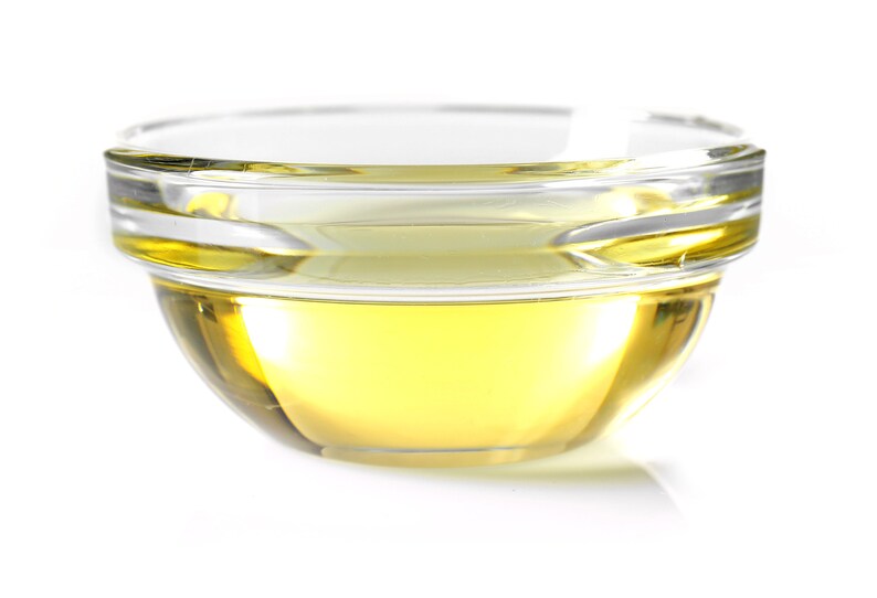 May include: A clear glass bowl filled with a golden yellow liquid, likely oil or vinegar, on a white background.